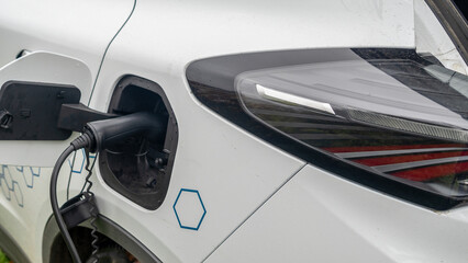 Fototapeta premium Close-up view of power supply plugged into an electric car being charged. White electric car charging.