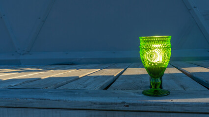Illuminated empty glasses of green glass on a stem on a wooden background. Close-up view.