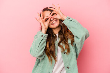 Young caucasian woman isolated on pink background showing okay sign over eyes