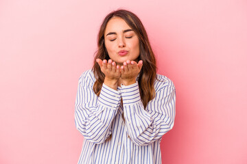 Young caucasian woman isolated on pink background folding lips and holding palms to send air kiss.