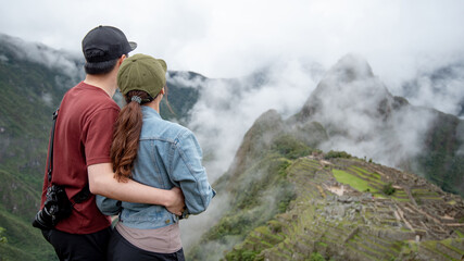 Asian couple tourist looking at Machu Picchu, one of seven wonders and famous tourist attraction in Cusco Region of Peru. This majestic place has known as 'Lost City of the Incas'
