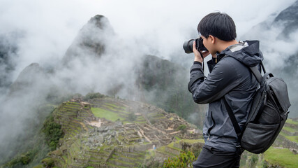 Asian man traveler and photographer taking photo at Machu Picchu, one of seven wonders and famous...