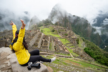 Asian woman traveler raising hand at Machu Picchu, one of seven wonders and famous tourist attraction in Cusco Region of Peru. This majestic place has known as 'Lost City of the Incas'