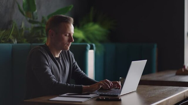 Handsome freelancer businessman in glasses diligently working on laptop in cafe. Man typing on keyboard and searches new job on internet at coffee shop. Business concept