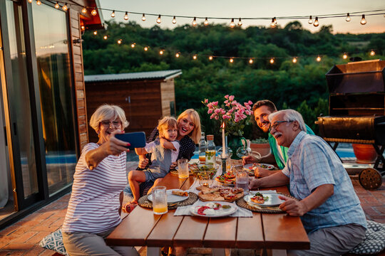 Happy senior woman and her cheerful family taking selfie during dinner in the backyard