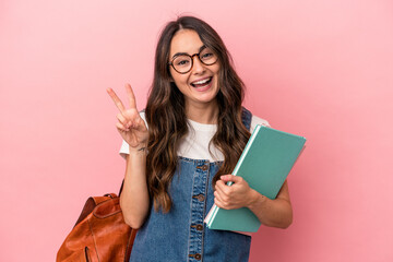 Young caucasian student woman isolated on pink background joyful and carefree showing a peace symbol with fingers.