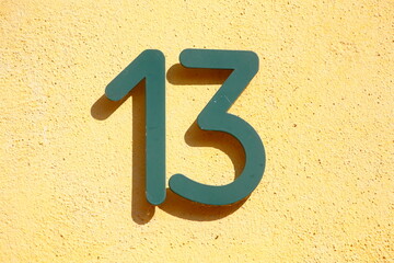 Grünes Hausnummernschild Nr. Dreizehn auf  gelber Hauswand, Deutschland, Europa