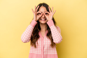 Young caucasian woman isolated on yellow background showing okay sign over eyes