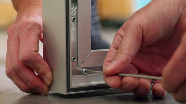 Two workers assemble a metal frame.Allen screws are screwed into the frame with an Allen key.
