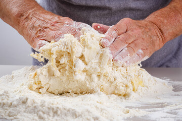 Female hands of an elderly woman knead the dough on a gray table. Senior woman in a gray apron preparation of dough for a pizza, bread, pasta, festive cake. Shallow depth of field