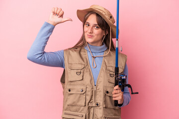 Young caucasian fisherwoman holding a rod isolated on pink background feels proud and self confident, example to follow.