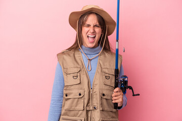 Young caucasian fisherwoman holding a rod isolated on pink background screaming very angry and aggressive.