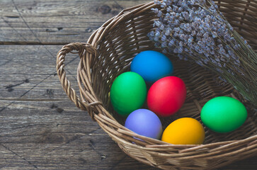 Colored easter eggs in wicker basket with a bunch of lavender on wooden surface