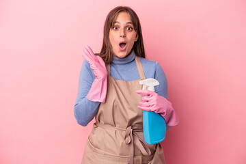 Young caucasian cleaner woman holding spray isolated on pink background surprised and shocked.