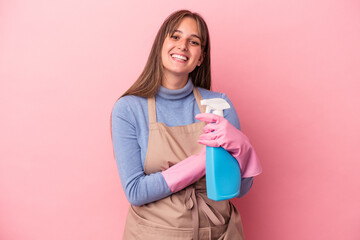 Young caucasian cleaner woman holding spray isolated on pink background laughing and having fun.
