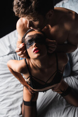 Top view of shirtless man wearing lace mask on sensual girlfriend on bed isolated on black