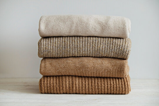 Bunch of knitted warm pastel color sweaters with different knitting patterns folded in stack, clearly visible texture. Stylish fall-winter season knitwear clothing. Close up, copy space for text.