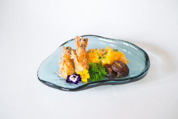 Two shrimps in batter with sauce and mushrooms on the blue designed plate. Deep fried prawns decorated with greenery and flower. Isolated on white