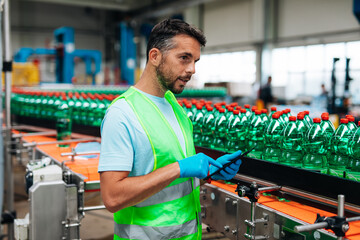 Male worker in bottling factory checking water bottles before shipment. Inspection quality control.