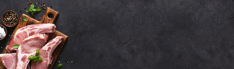 Raw pork steaks on a board with spices and basil on a dark background. Top view. Fresh meat. Ribs.