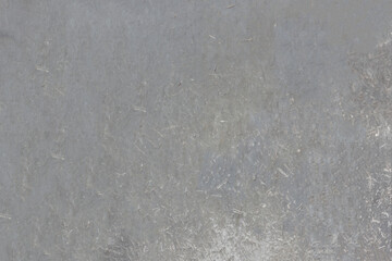 The weathered surface of the chipboard sheet, faded under the sun. Mottled structure with fine speckles.