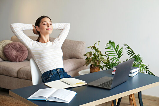 Young beautiful woman with blissful facial expression taking a break at the office to meditate. Brunette female relaxing on a chair by her workspace at lunch time. Close up, copy space, background
