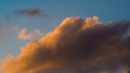 Naklejka na ściany i meble Zoom sur un cumulus illuminé par une lumière orangée, pendant le coucher du soleil