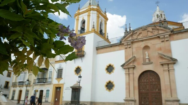 The beautiful church in the famous "Plaza del Socorro" (meaning: "Square of Assistance"), in Ronda, Andalusia, Spain. Green leaves in the foreground. Blurred tourists in the background.