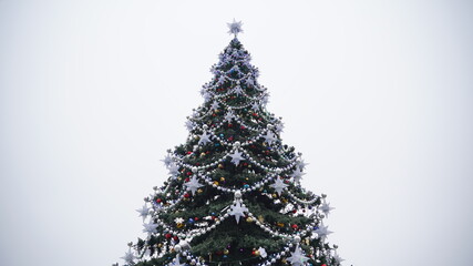 Christmas tree with different christmas toys against cloudy sky in downtown. Coniferous tree with decorative adornments to create festive mood during holidays.