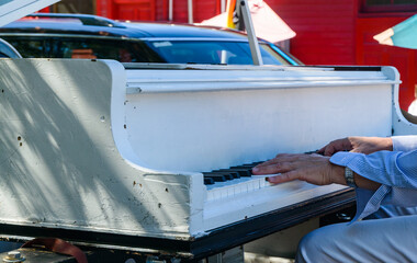 Hands Playing the Keys of a White Piano on the Bed of a Pickup Truck
