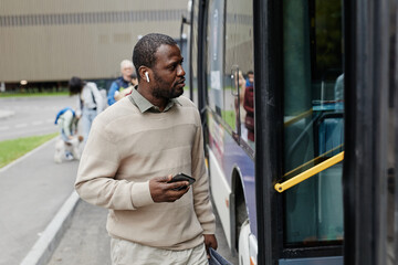 Waist up portrait of adult African-American man entering bus at bus stop in city, copy space