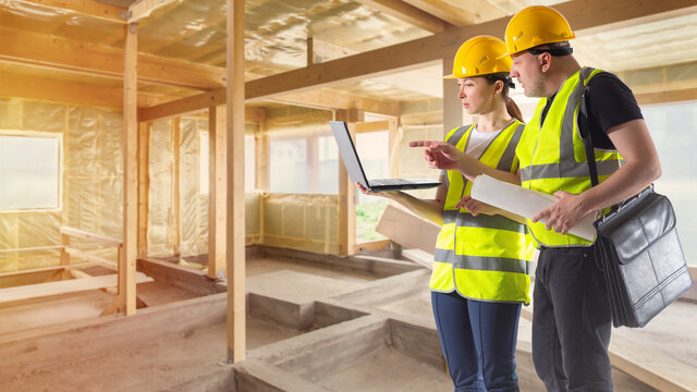 Two builders are discussing something. Builders meeting concept. Builders meeting with laptop. They are inside house under construction. Construction company employees. People in building uniform - Powered by Adobe