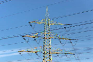 Power lines and pylons for transmission of electricity, against a blue sky background.