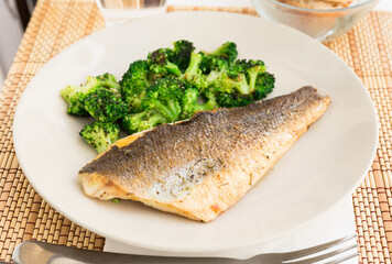 fried fillet of sea bass with garnish of broccoli on black warm stone plate