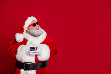 Photo of dreamy old man hold telephone look empty space wear santa hat costume isolated red color background