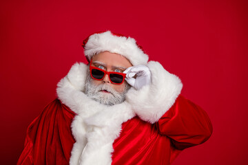 Portrait of attractive funny comic moody amazed stunned Santa touching specs isolated over vibrant red color background