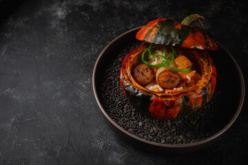 Baked pumpkin with rice and scalloped fish for the fall table for Halloween. Dark stone background. Holiday risotto.