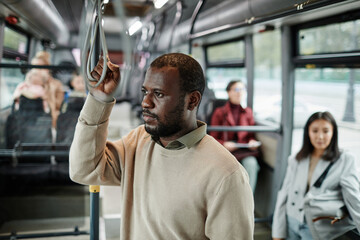 Waist up portrait of African-American man holding onto handle in bus while traveling by public transport in city, copy space
