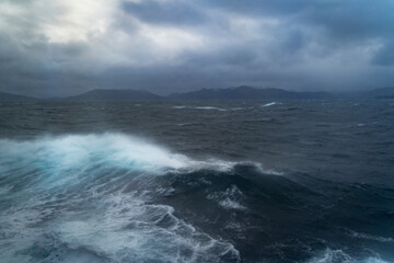 Wellen auf der Reise mit dem Schiff zum Nordkap, Norwegen. Sturm auf dem Atlantik mit Schaumkronen auf den Wellen und Gischt auf dem Schiff. dunkle Wolken werden vom Wind über das Meer gejagt. Ozean