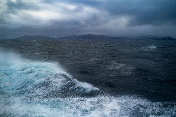 Wellen auf der Reise mit dem Schiff zum Nordkap, Norwegen. Sturm auf dem Atlantik mit Schaumkronen auf den Wellen und Gischt auf dem Schiff. dunkle Wolken werden vom Wind über das Meer gejagt. Ozean