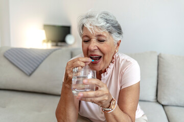 Unhealthy middle aged woman suffers from pain, holding pill and glass of still water feels ill taking medicine, cropped image. Disease prevention and treatment of old mature people concept.