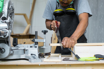 A young male carpenter cutting the wood using hand saw on his workshop table wearing safety equipment