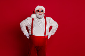 Fototapeta na wymiar Photo of confident positive cheerful overweight man hands hips wear santa hat costume isolated red color background