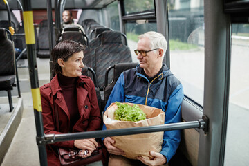 Portrait of adult couple chatting in bus while traveling by public transport in city, copy space