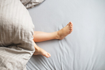 child sleep in the bed. baby's feet stick out from under the blanket