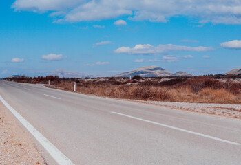 Asphalt road goes to the horizon. Landscape view perspective of road with white clouds on blue sky. Traveling by car. Trendy background for branding, calendar, multicolor card, banner, cover, header