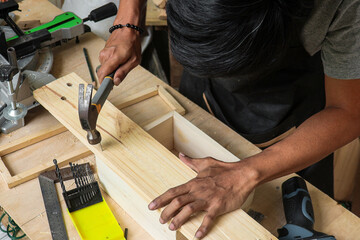 A young male carpenter working on his workshop table using hammer 