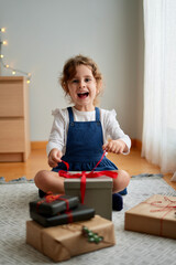 Happy little girl sitting on the floor opening the box with the Christmas gift. Cocept Holiday, Christmas, New Year.