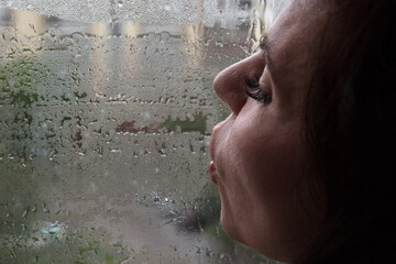 sad woman blows air with her lips on window fogged from the rain. The concept of autumn melancholy depression.