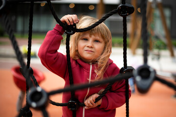 Little girl 5 years old blonde in red clothes plays on the playground